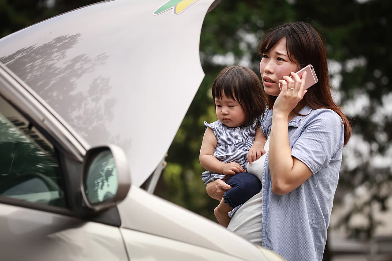 車のフロントを開けて困った様子で電話をしている女性